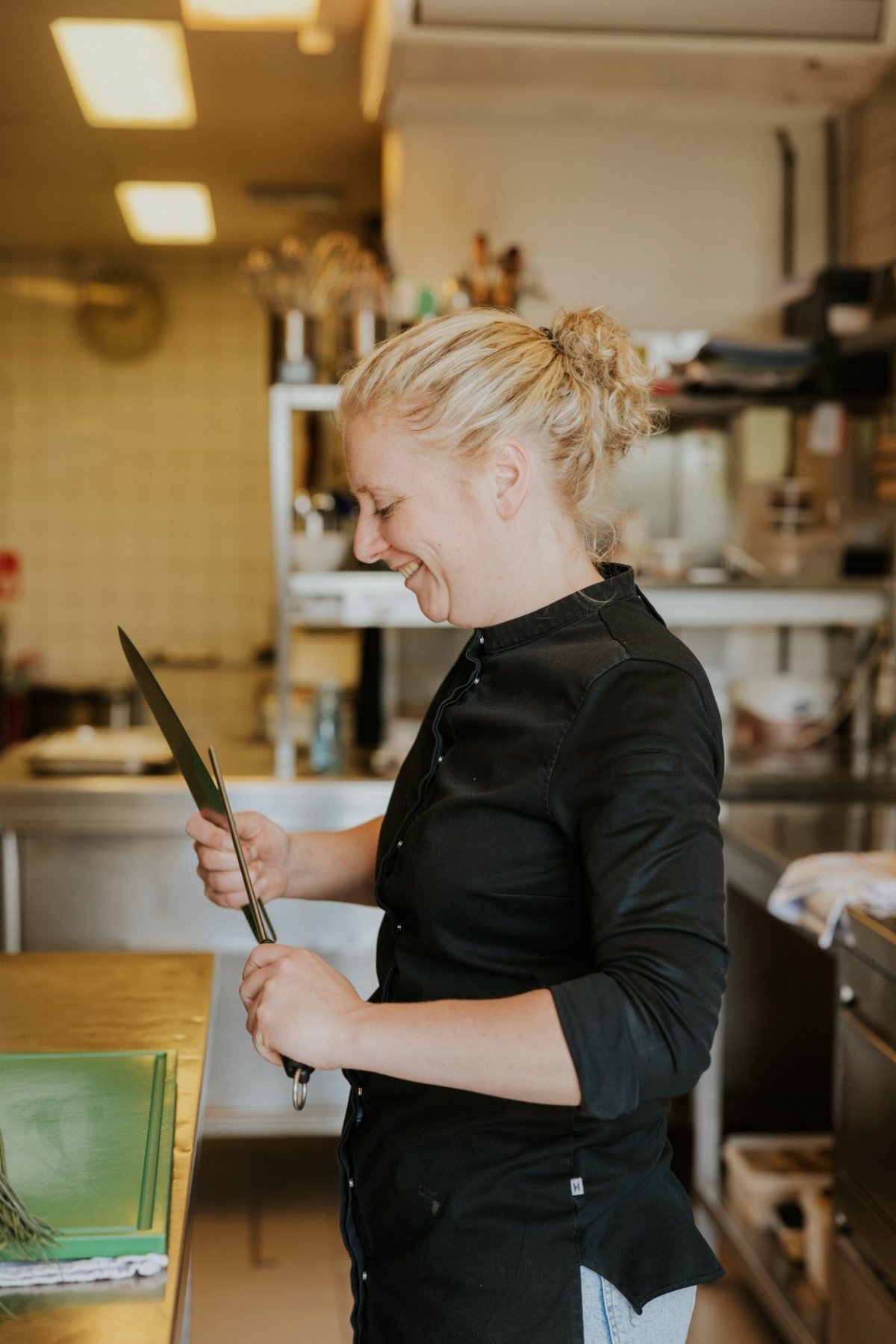 vrouwlijke chef, met zwarte vest is mes aan het slijpen
