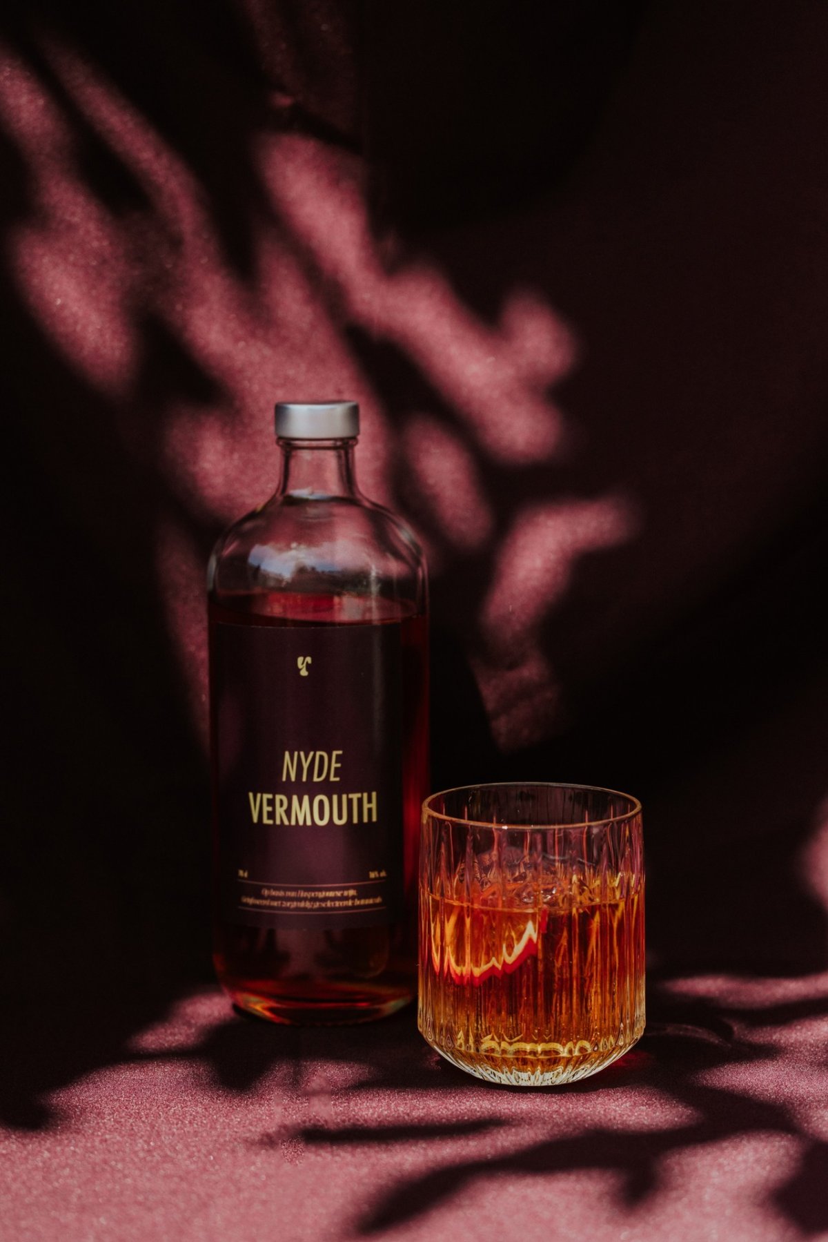 close-up foto van een fles vermouth met een glas erbij, dit staat op een paarse achtergrond