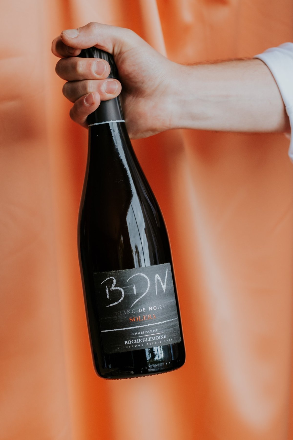 Close-up van een donkere fles, op een oranje achtergrond op het etiket staat er BDN Solera champagne
